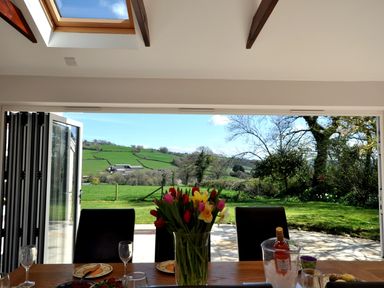 A dining table with flowers glasses and plates overlooking an open garden and green hills at Culverwells in Axminster