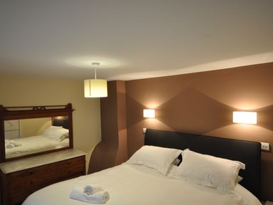 A bedroom with a double bed white linens two rolled towels on the bed a wooden dresser with a mirror and wall and ceiling lights at Culverwells in Axminster