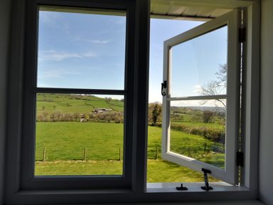 A window open to a view of green fields and hills with some trees and buildings in the distance at Culverwells Axminster