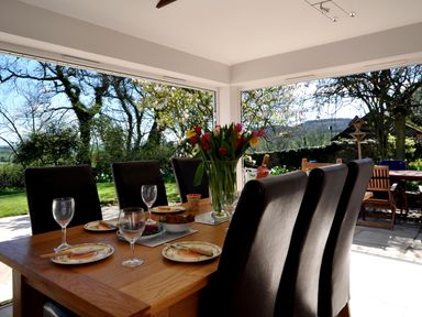 A dining room with a wooden table set with plates glasses and a vase of flowers overlooking a garden at Culverwells Axminster