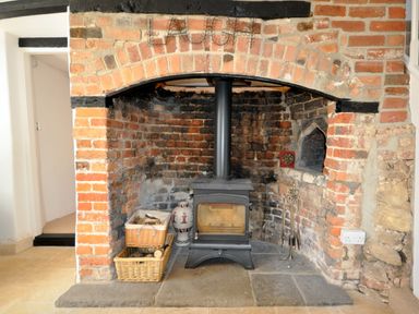 A brick fireplace with a wood burning stove baskets of firewood and fireplace tools at Culverwells in Axminster