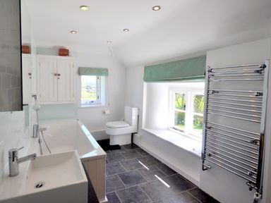 A bathroom with a bathtub a sink a toilet a wall cabinet and a chrome towel radiator at Culverwells in Axminster