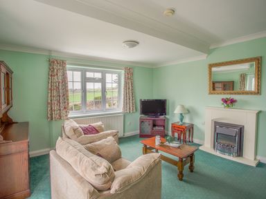 A living room with two couches, a wooden coffee table, TV on a stand, a fireplace with a mirror above it, and floral curtains at The Doves in Burton Bradstock