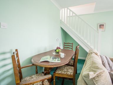 A dining area with a wooden table and chairs under a staircase next to a sofa at The Doves in Burton Bradstock