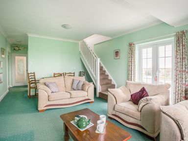 A living room with beige sofas a wooden coffee table with a teapot and cups green carpet and curtains floral pattern at The Doves in Burton Bradstock