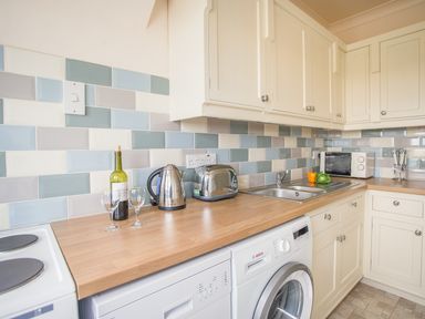 A kitchen countertop with a kettle toaster wine bottle two glasses sink microwave and washing machine at The Doves in Burton Bradstock