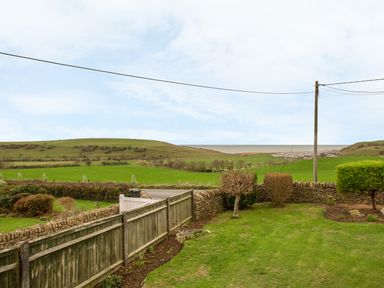 A garden with bushes and a wooden fence overlooking green fields and a distant coastline at The Doves in Burton Bradstock