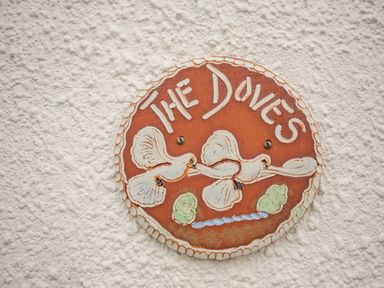 A circular ceramic sign with two doves and the words The Doves on a textured white wall at The Doves in Burton Bradstock