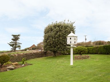 A garden with a large white birdhouse on a post surrounded by trees and shrubbery at The Doves in Burton Bradstock