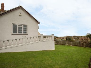 The side of a white house with a large grass lawn and a white balustrade at The Doves in Burton Bradstock