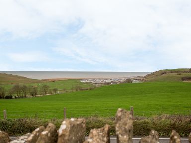 A green field with hills and trees overlooking a coastal settlement and the sea at The Doves in Burton Bradstock