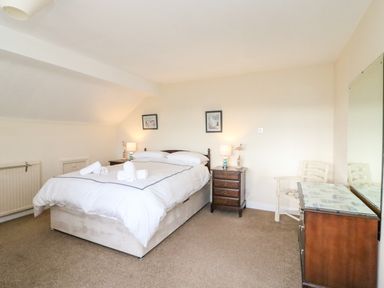 A bedroom with a double bed and bedside tables with lamps and a chair next to a dresser with a mirror at The Doves in Burton Bradstock