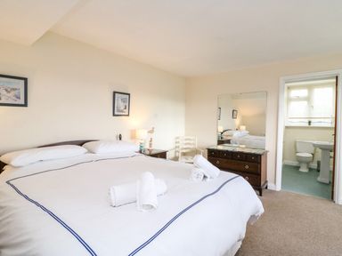 A bedroom with a bed two nightstands a chair a dresser with a mirror and an ensuite bathroom at The Doves in Burton Bradstock