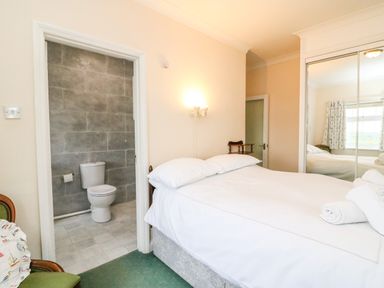 A bedroom with a double bed towels a chair and an ensuite bathroom with a toilet at The Doves in Burton Bradstock
