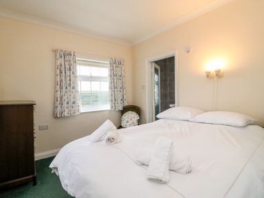 A bedroom with a bed with white linens and towels a window with patterned curtains a wooden dresser and a chair at The Doves in Burton Bradstock