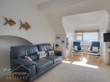 A living room with a blue leather sofa, two blue armchairs, a window with a sea view, and wall decorations at Dream View in Greenhill
