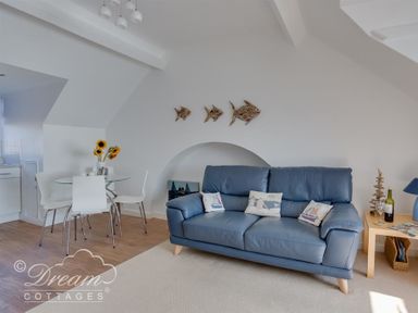 A living room with a blue sofa and nautical cushions next to a glass dining table with white chairs and sunflowers at Dream View in Greenhill
