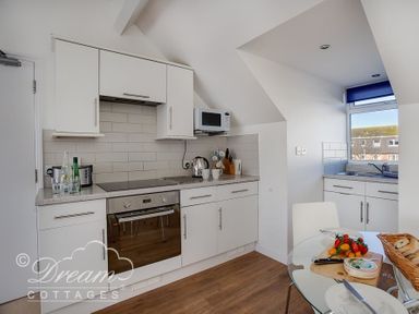A kitchen with white cabinets a built in oven a microwave kettle and a glass table with food at Dream View in Greenhill