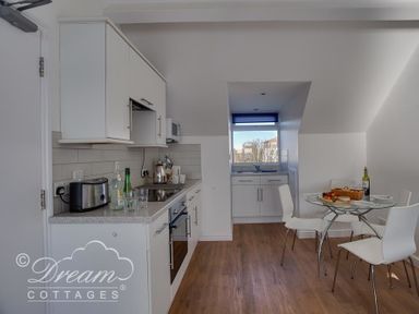 A kitchen with white cabinets a toaster bottles and glasses on the counter a glass dining table with white chairs and food at Dream View in Greenhill