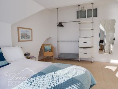 A bedroom with a bed a chair a wall-mounted open wardrobe and a wavy wall mirror at Dream View in Greenhill