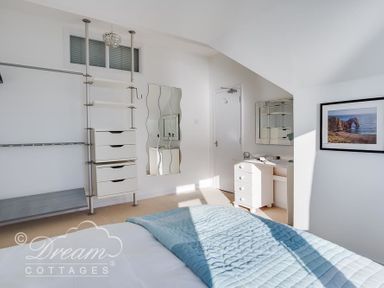 A bedroom with a blue quilt on the bed a white dresser a wavy mirror and a wall photo at Dream View in Greenhill