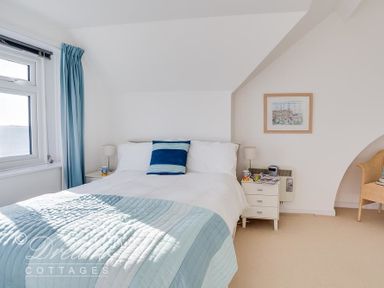 A bedroom with a double bed blue and white bedding nightstands with lamps a window with blue curtains and a wicker chair at Dream View in Greenhill