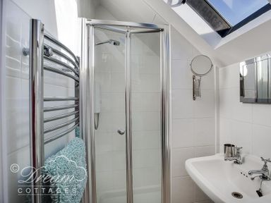 A bathroom with a shower enclosure a wall-mounted mirror a towel rack with towels and a sink under a skylight at Dream View in Greenhill