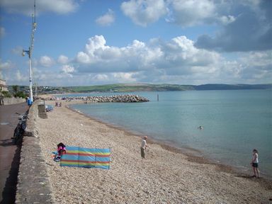 A pebble beach with people near the shore and a stone wall with lamp posts at Dream View in Greenhill