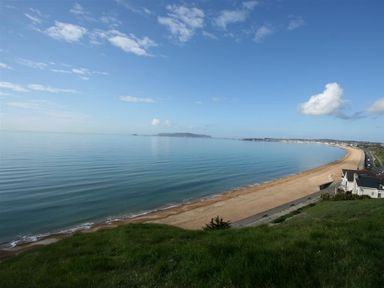 A beach with a sandy shore and calm sea bordered by grass and houses at Dream View in Greenhill