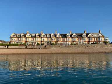 A row of seaside houses with a pebble beach and calm sea in front at Dream View in Greenhill