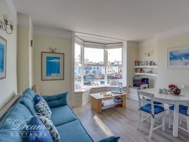 A living room with blue sofa white dining table with blue cushions and a bay window with a seating area at Harbour Edge in Brewers Quay Harbour