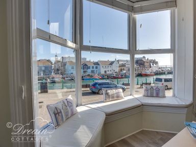 A bay window seating area with cushions overlooking a street and waterfront at Harbour Edge in Brewers Quay Harbour
