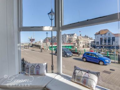 A bay window with cushions looking out onto a street with parked cars and buildings at Harbour Edge Brewers Quay Harbour