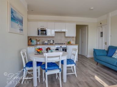 A kitchen with white cabinets and appliances a round white dining table with four chairs with blue cushions and a blue sofa in Brewers Quay Harbour