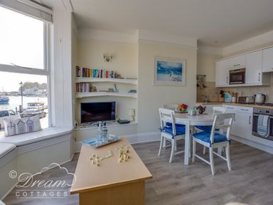 A dining area with a round table and chairs next to a kitchen with white cabinets and a window seat overlooking a harbor at Harbour Edge Brewers Quay Harbour