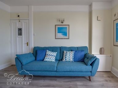 A blue sofa with patterned and plain cushions in a room with a white door and framed pictures at Harbour Edge Brewers Quay Harbour