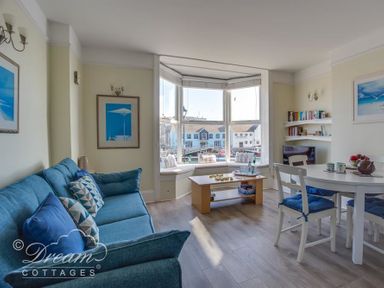 A living room with a blue couch, coffee table, dining table with chairs, and a large bay window at Harbour Edge Brewers Quay Harbour