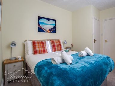 A bedroom with a double bed blue blanket and red plaid pillows two bedside tables and a picture of a heart shaped beach scene on the wall at Harbour Edge in Brewers Quay Harbour