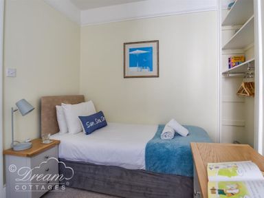 A small bedroom with a single bed side table lamp open closet and framed picture on wall at Harbour Edge Brewers Quay Harbour