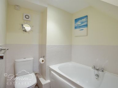 A bathroom with a toilet a bathtub a round mirror and a beach painting at Harbour Edge Brewers Quay Harbour