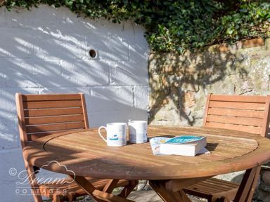 An outdoor patio with a round wooden table two wooden chairs two mugs and a book at Harbour Edge in Brewers Quay Harbour
