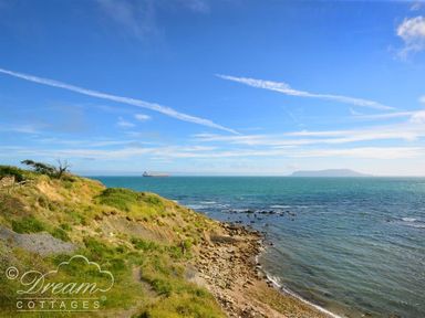A coastline with grassy cliffs and a rocky shore overlooking the sea with a ship in the distance at Harbour Edge in Brewers Quay Harbour