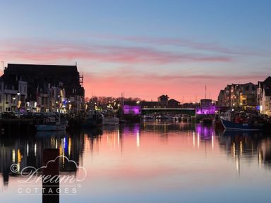A harbor with boats docked along buildings under a colorful sunset sky at Harbour Edge Brewers Quay Harbour