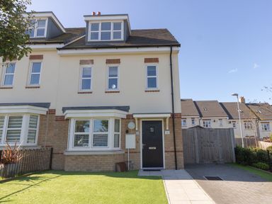 A semi detached house with black front door and multiple windows with a green lawn and paved driveway at The Ferns in Weymouth