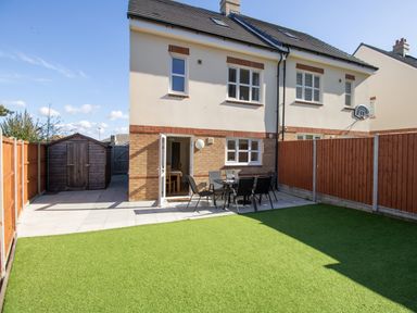 A backyard with artificial grass a patio area with a table and chairs a wooden shed and a basketball hoop on a house at The Ferns in Weymouth