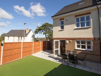 A backyard with artificial grass, patio furniture, and a two-story house at The Ferns in Weymouth