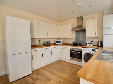 A kitchen with white cabinets wooden countertops a fridge oven microwave washing machine and a sink at The Ferns in Weymouth