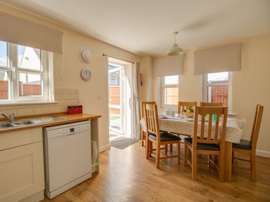 A dining area with a wooden table and chairs next to a kitchen with a sink and dishwasher at The Ferns in Weymouth