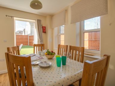 A dining area with a wooden table and chairs set with dishes and fruit bowl at The Ferns in Weymouth