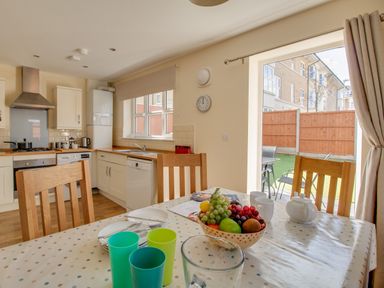 A kitchen with wooden chairs a table with cups plates and a fruit bowl at The Ferns in Weymouth